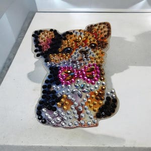 Calamita da frigo completamente tempestata di gemme. Calamita da frigo tempestata di diamanti, diamantè e grandi cristalli, a forma di piccolo cagnolino carino con papillon rosa.