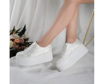 May include: White platform sneakers with a floral embroidered design. The sneakers have a thick white platform sole and lace-up closure.
