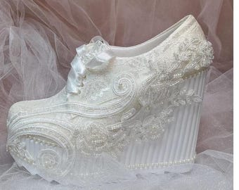 May include: White lace wedge shoe with floral and swirl patterns, adorned with pearls and a satin bow. The platform wedge heel is approximately 4 inches high, with a textured design.