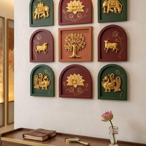 May include: A set of nine wall-mounted decorative panels featuring gold-coloured relief sculptures of elephants, lotus flowers, a tree, cows, and peacocks. The panels are arranged in a grid, with arched and square frames in dark green and maroon.
