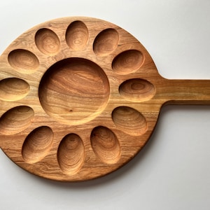 May include: A wooden serving tray with a handle and 12 individual indentations for holding eggs or other small snacks. The tray is made of light brown wood with a natural grain pattern.