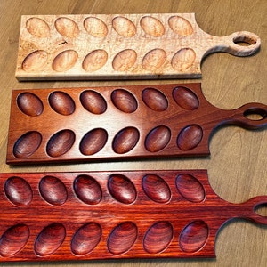 May include: Three wooden egg trays with handles. The top tray is light wood with a natural finish. The middle tray is dark brown wood with a polished finish. The bottom tray is a deep red wood with a polished finish.