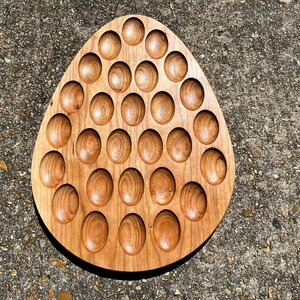 May include: A wooden egg-shaped tray with 42 round depressions, perfect for holding small items like marbles or buttons.