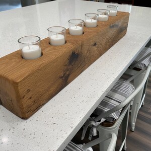 May include: A rustic wooden candle holder with six glass candle holders. The candle holder is made of reclaimed wood and has a natural finish. The candle holders are arranged in a row and are filled with white candles.