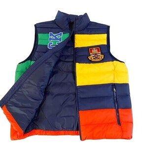 Könnte beinhalten: Eine blaue, grüne, gelbe und rote Steppweste mit Reißverschluss. Die Weste hat einen großen Aufnäher auf der Vorderseite mit dem Text "Ralph Lauren" und einem Wappen.