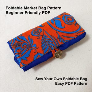May include: Foldable market bag pattern. The bag is folded and closed, showing an orange fabric with blue floral designs. The bag has a blue border and is secured with a button. Text on the image reads: "Foldable Market Bag Pattern Beginner Friendly PDF" and "Sew Your Own Foldable Bag Easy PDF Pattern."