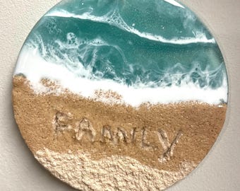 May include: Round, resin ornament with a blue and white ocean wave design and a sandy beach bottom. The word "FAMILY" is written in the sand.