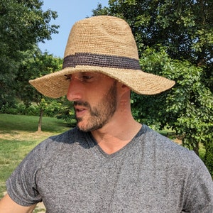 Peut inclure: Un chapeau de paille à larges bords avec une bande noire. Le chapeau est fait d'un matériau naturel et a une couronne légèrement affaissée.