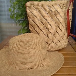 May include: A woven straw hat with a wide brim and a matching backpack with leather straps. The hat is lying on a wooden surface next to the backpack. The backpack has a diagonal pattern.