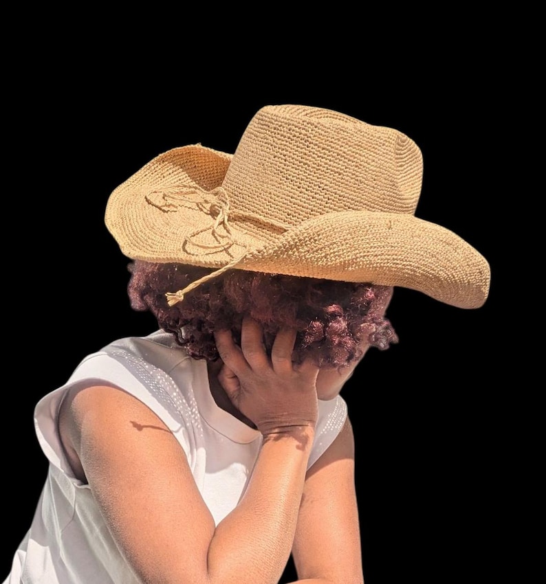 Pode incluir: Uma pessoa usando um chap&eacute;u de cowboy de palha marrom com uma fita marrom. A pessoa est&aacute; usando uma camisa branca sem mangas e tem a cabe&ccedil;a baixa.