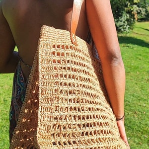 K&ouml;nnte beinhalten: Eine gro&szlig;e, braune, geflochtene Strohtasche mit einem Lederriemen. Die Tasche hat ein Gittermuster und ist perfekt f&uuml;r den Transport von Alltagsgegenst&auml;nden.