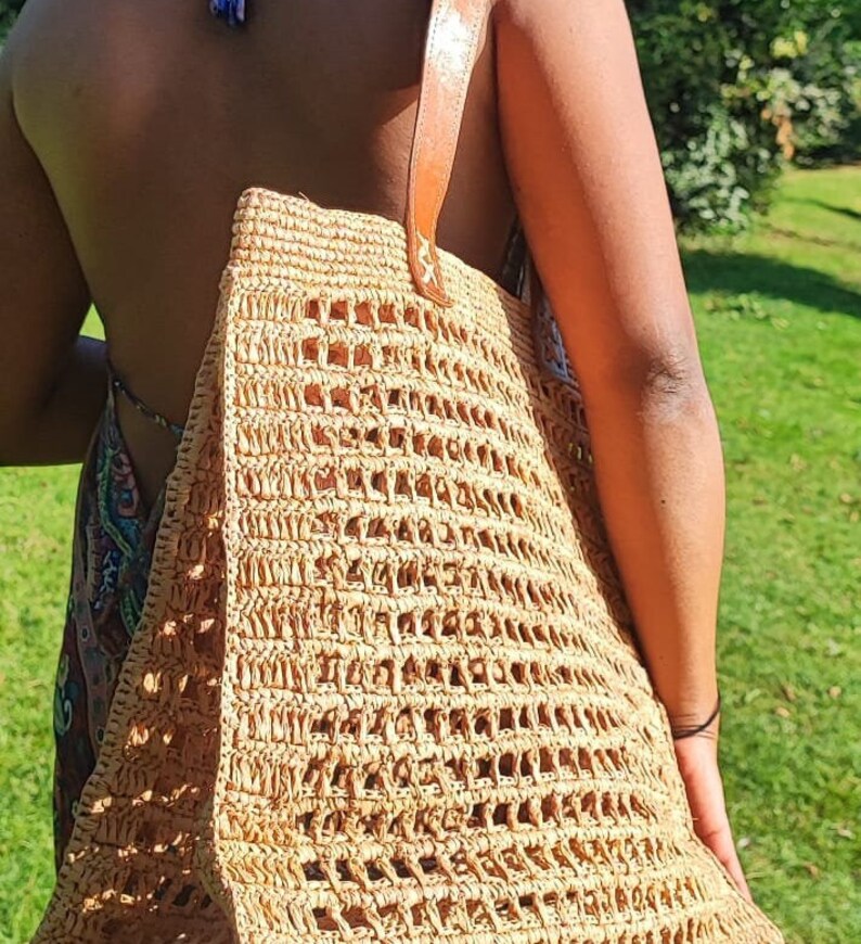 K&ouml;nnte beinhalten: Eine gro&szlig;e, braune, geflochtene Strohtasche mit einem Lederriemen. Die Tasche hat ein Gittermuster und ist perfekt f&uuml;r den Transport von Alltagsgegenst&auml;nden.