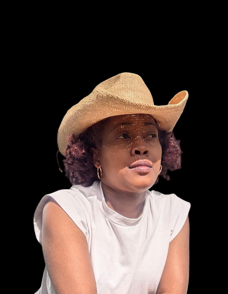 Pode incluir: Uma mulher com cabelo castanho encaracolado vestindo uma camiseta branca e um chap&eacute;u de cowboy marrom claro.