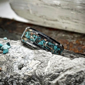 May include: A silver ring with a turquoise inlay. The ring is set on a white and gray rock.