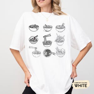 May include: White t-shirt with a black and white illustration of nine bowls of ramen noodles. The bowls are arranged in a 3x3 grid pattern. The text "COMFORT COLORS WHITE" is in the bottom right corner of the image.