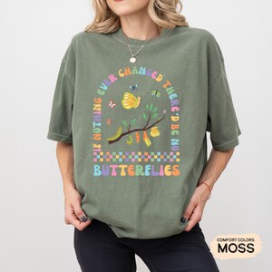 K&ouml;nnte beinhalten: Gr&uuml;nes T-Shirt mit einem Motiv eines Zweigs mit Schmetterlingen und Raupen. Der Text auf dem Shirt lautet "If nothing ever changed there'd be no butterflies".