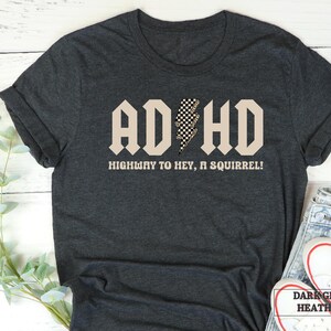 May include: Dark grey heather t-shirt with a black and white checkered lightning bolt graphic and the text "ADHD HIGHWAY TO HEY, A SQUIRREL!"