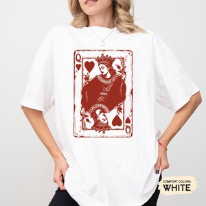 May include: White t-shirt with a red graphic of the Queen of Hearts playing card. The card features a stylized illustration of the Queen holding a heart and a crown.
