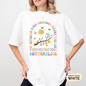 K&ouml;nnte beinhalten: Wei&szlig;es T-Shirt mit einem bunten Grafikdesign, das einen Zweig mit Schmetterlingen, Raupen und Kokons zeigt. Der Text "If nothing ever changed there'd be no butterflies" ist in einem Regenbogenbogen um die Grafik geschrieben.