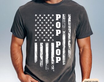 May include: A dark gray t-shirt with a distressed American flag design and the word "POP" vertically down the center of the flag.