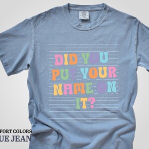 May include: A light blue t-shirt with the text "Did you put your name on it?" in colorful letters on a white background.