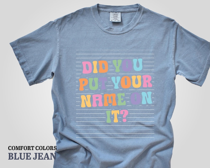 May include: A light blue t-shirt with the text "Did you put your name on it?" in colorful letters on a white background.