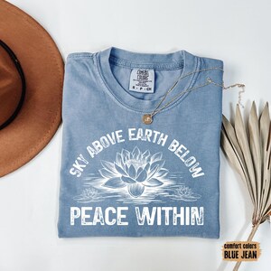 May include: A light blue t-shirt with a white graphic design featuring a lotus flower and the text "Sky Above Earth Below Peace Within".