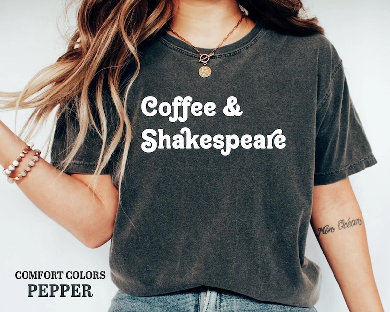 May include: A dark gray t-shirt with the text "Coffee & Shakespeare" in white. The shirt is made of a soft, comfortable material and has a relaxed fit.