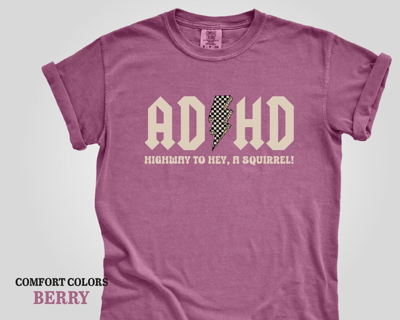 May include: A pink t-shirt with a white graphic that says "ADHD Highway to hey, a squirrel!" with a checkered lightning bolt.