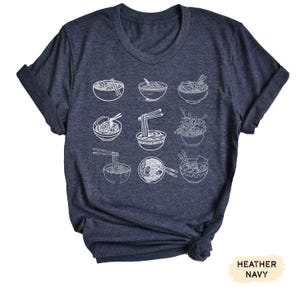 May include: A heather navy blue t-shirt with a white graphic of various bowls of ramen noodles.