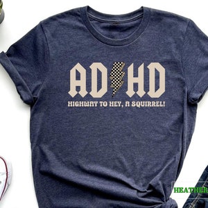 May include: Heather navy blue t-shirt with a beige graphic that says "ADHD Highway to Hey, a Squirrel!" with a black and white checkered lightning bolt.