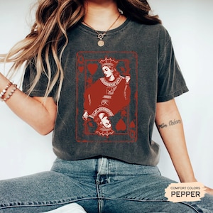 May include: A dark gray t-shirt with a red Queen of Hearts playing card graphic. The card features a red queen with a crown and a red heart in the corner. The text "COMFORT COLORS PEPPER" is visible in the bottom right corner.