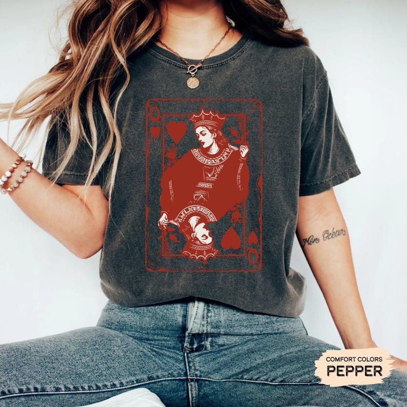 May include: A dark gray t-shirt with a red Queen of Hearts playing card graphic. The card features a red queen with a crown and a red heart in the corner. The text "COMFORT COLORS PEPPER" is visible in the bottom right corner.