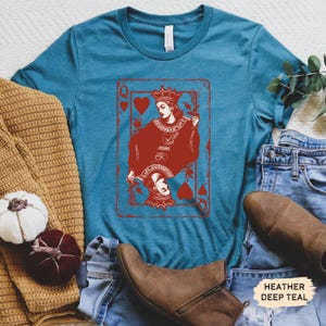 May include: A teal blue t-shirt with a red graphic of the Queen of Hearts playing card. The text "HEATHER DEEP TEAL" is visible in the bottom right corner of the image.