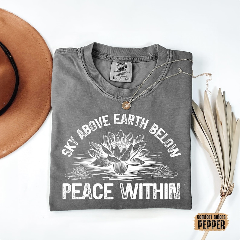 May include: Gray t-shirt with a white graphic that says "Sky Above Earth Below Peace Within". The graphic also features a stylized lotus flower.