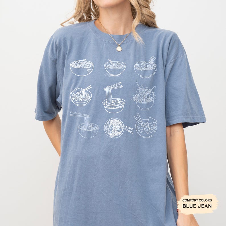 May include: A blue jean t-shirt with a white graphic of nine bowls of ramen noodles. The bowls are arranged in a 3x3 grid pattern. The t-shirt has a crew neck and short sleeves.