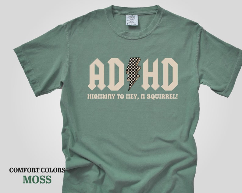 May include: A moss green t-shirt with a white graphic that says "ADHD" with a checkered lightning bolt in the middle. The text below the graphic says "Highway to hey, a squirrel!"