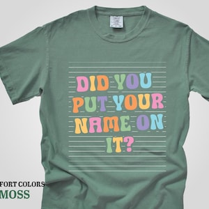May include: A green t-shirt with the text "Did you put your name on it?" in colorful letters on a white background.