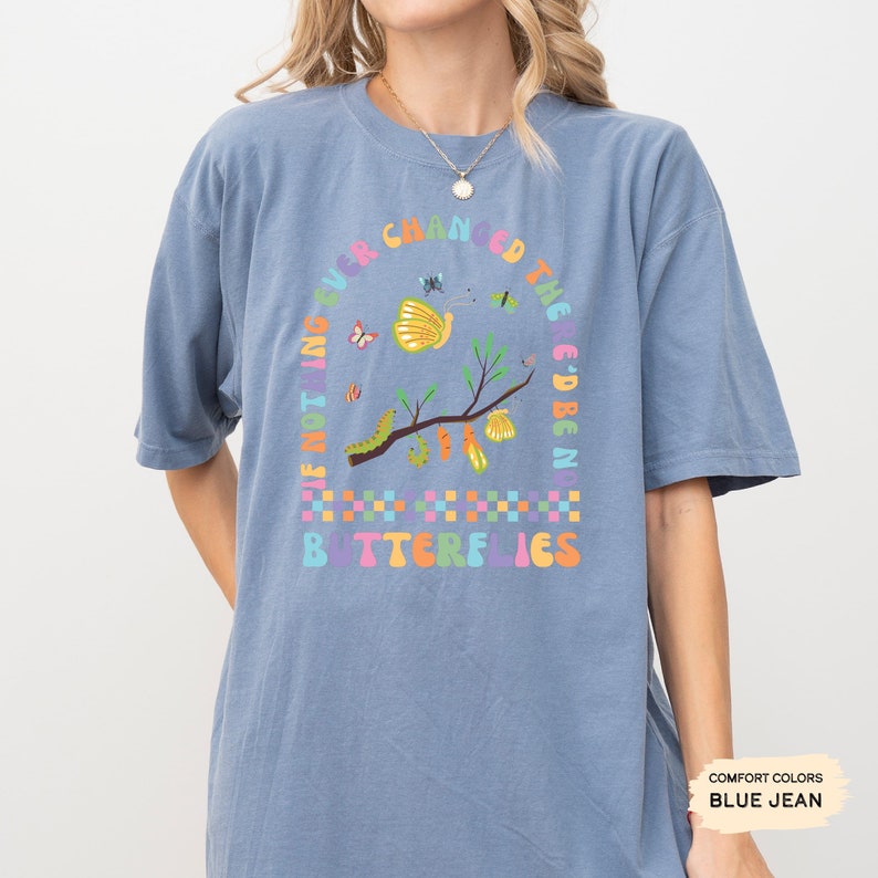 K&ouml;nnte beinhalten: Ein blaues T-Shirt mit einem Motiv eines Zweigs mit Schmetterlingen und Raupen. Der Text "Wenn sich nichts jemals &auml;ndern w&uuml;rde, g&auml;be es keine Schmetterlinge" ist um das Motiv herum geschrieben.