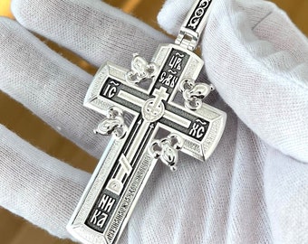 May include: A silver cross pendant with black enamel detailing and Cyrillic lettering. The cross features intricate designs and a bail with a loop for attaching a chain.