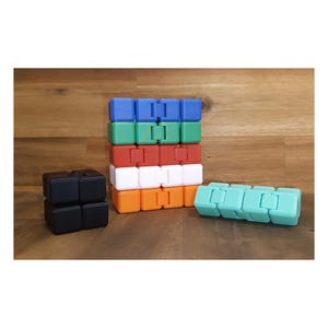 Könnte beinhalten: Eine Sammlung von Fidget-Infinity-Cubes in verschiedenen Unifarben, darunter Schwarz, Blau, Grün, Rot, Weiß, Orange und helles Türkis. Die Würfel bestehen aus mehreren kleinen quadratischen Segmenten, die durch Scharniere miteinander verbunden sind.