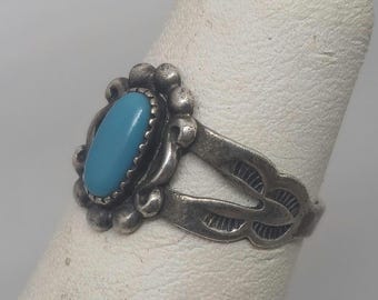 May include: A silver ring with a turquoise stone set in a floral design.