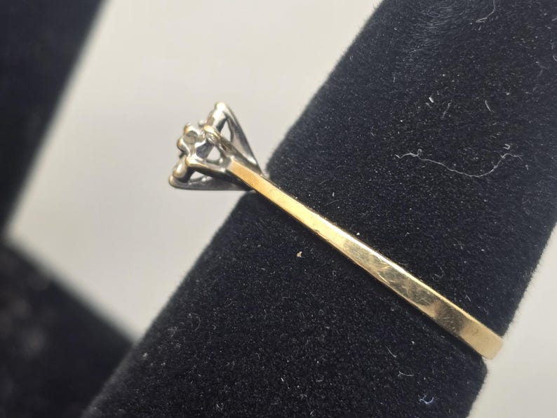 May include: A two-tone ring featuring a yellow gold band that transitions into a silver-toned setting. The setting holds a single, small, clear, faceted stone in a prong mount, showcasing a classic design with a polished metal finish.
