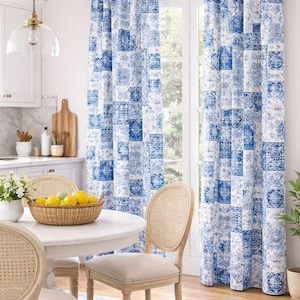 Può includere: Tende a fantasia blu e bianca in una cucina luminosa. Le tende presentano un design patchwork con vari motivi geometrici e floreali. Un tavolo rotondo bianco con sedie in vimini e un cesto di limoni completano la scena.