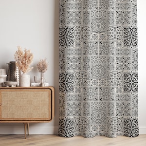 以下が含まれることがあります： 黒と白のタイル模様が繰り返される柄のカーテン。各タイル内には、華やかな花柄と幾何学模様が施され、視覚的に豊かで質感のある外観を作り出しています。カーテンは壁の前に吊るされています。