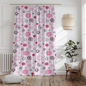 以下が含まれることがあります： ピンク、グレー、濃いピンクの円、花、スパイラルデザインの繰り返し模様が施された白いカーテン。カーテンは窓の前に吊り下げられており、デザインは生地全体に見えます。