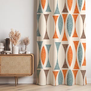 May include: Cream-coloured curtain featuring a repeating geometric pattern in orange, teal, and brown. The design includes elongated, hourglass-like shapes. The curtain hangs in front of a white wall.