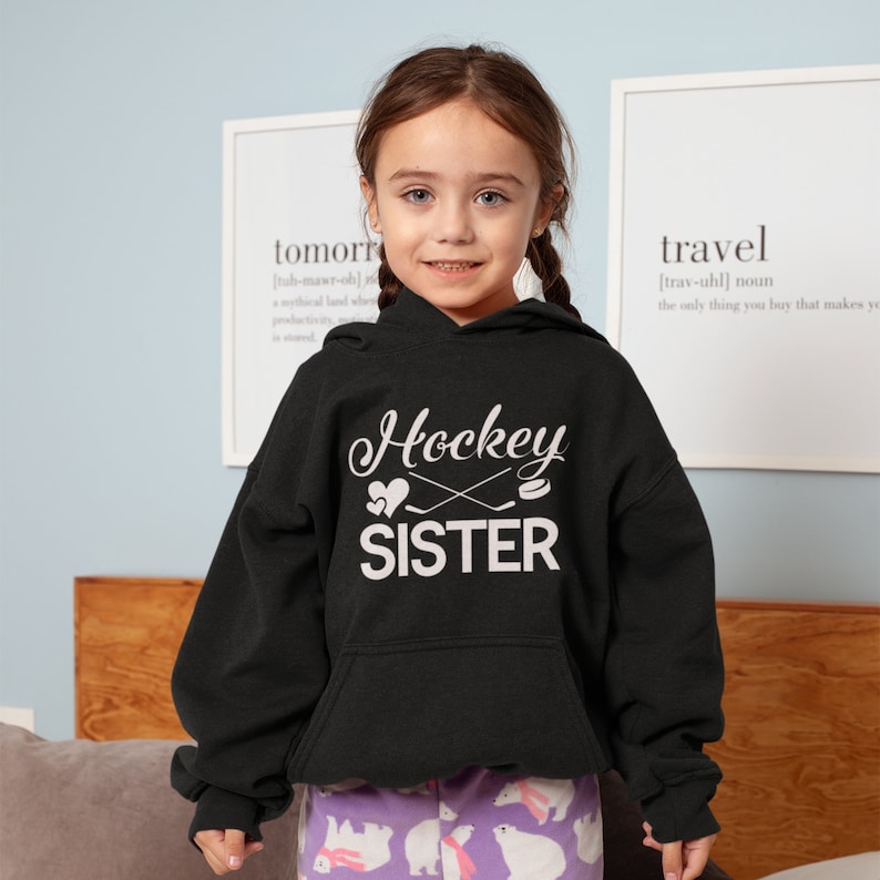 May include: A black hoodie with a white graphic that says "Hockey Sister" with a hockey stick and puck design. The hoodie has a drawstring hood and a kangaroo pocket.
