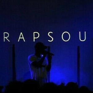 Puede incluir: Una persona cantando en un escenario frente a un fondo azul oscuro con la palabra "TRAPSOUL" en letras blancas.