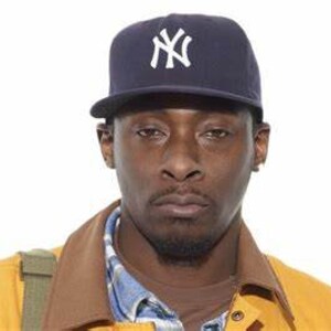 May include: A man wearing a navy blue baseball cap with a white "NY" logo. He is wearing a yellow jacket over a plaid shirt.